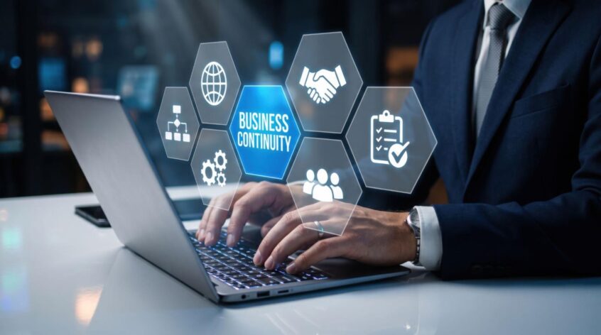 Professional working on a laptop with digital business continuity and risk management icons displayed on screen.